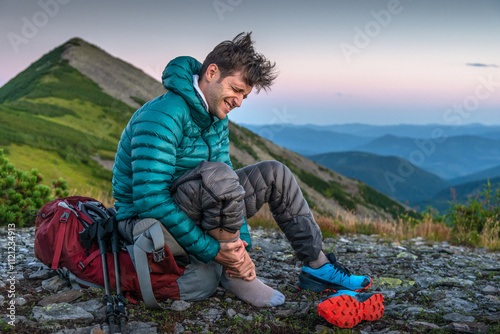 Man is Traveling with Backpack and has Problems with Sprained Ankle in the Mountains. Man with ankle injury feels pain in leg with an expression of pain on his face.
