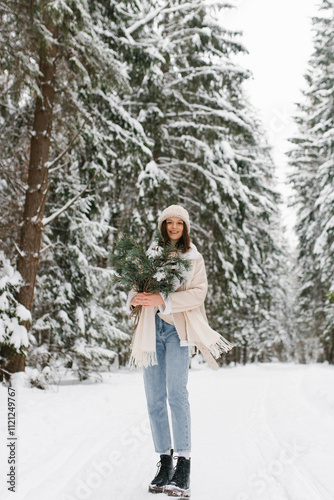 Smiling woman is standing in snow with scarf wrapped around her neck and pair of blue jeans. Concept of warmth and coziness