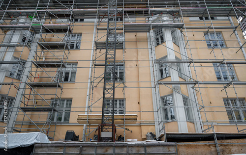 Scaffolding surrounding a beige building under renovation, featuring large windows and an industrial urban setting. Concept of construction photo