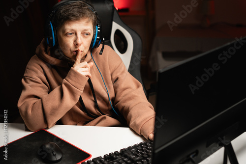 Portrait of female gamer play online video game on pc and showing the camera a gesture of silence. She closes mouth with finger. photo