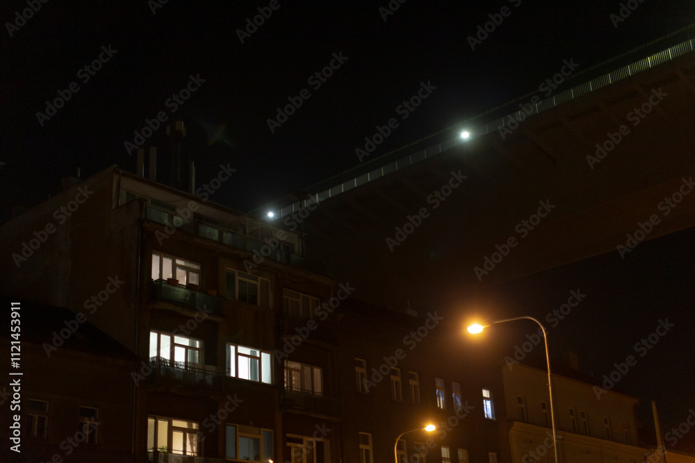 A street light shines brightly in front of a tall building during the dark of night, illuminating the surroundings with its glow A street light shines brightly in front of a tall building during the dark of night, illuminating the surroundings with its glow