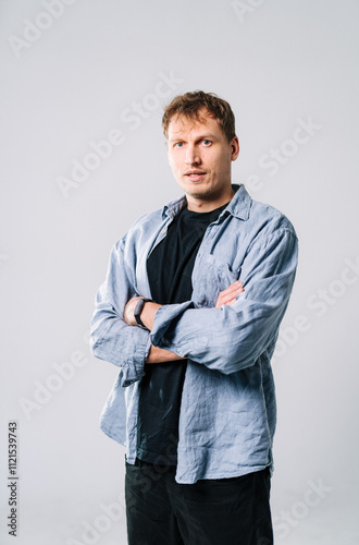 Man with crossed arms poses in a simple studio. Individual stands confidently with arms crossed, wearing a casual outfit in a minimalist studio setting.