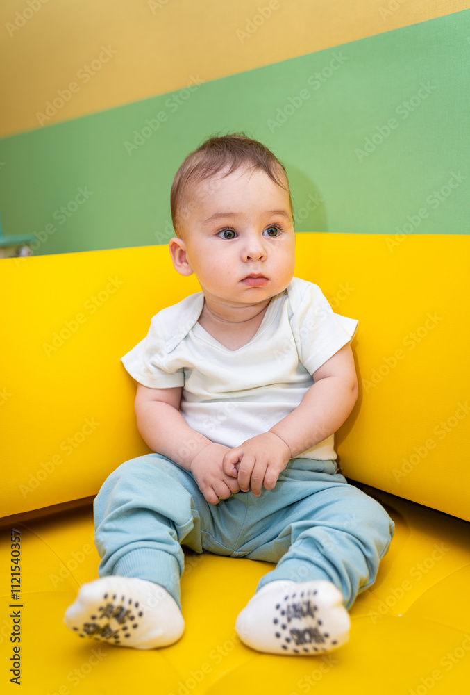 Baby on colorful cushion playfully. A curious baby sits calmly on a bright yellow cushion, surrounded by colorful walls, exploring the vibrant atmosphere. Baby on colorful cushion playfully. A curious baby sits calmly on a bright yellow cushion, surrounded by colorful walls, exploring the vibrant atmosphere.