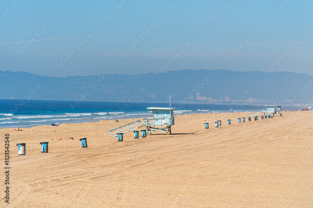 Californian beach near Los Angeles with typical lifeguard huts, tourists suntaning and garbage bins aligned on the sand