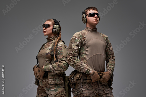 A male and female tactical duo stand back-to-back in military camouflage, exuding teamwork and strength.Wearing protective gear, gloves, and headphones, they embody readiness and modern combat skills.