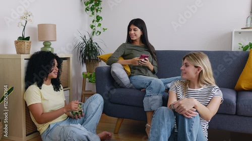 Happy young female student roommates meeting at home having fun telling stories, having lunch, spending time together. Millennial friends talking in the living room. Domestic lifestyle concept photo