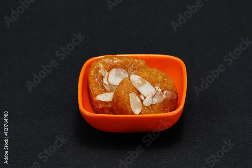 In a petite bowl of saffron color, there are two pieces of Mohanthal, which is a renowned sweet treat from Gujarat photo