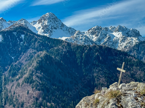 Selective focus of wooden summit cross of mountain peak Monte Nebria with panoramic view of snow capped ridges Julian Alps, Friuli Venezia Giulia, Italy. Wanderlust in alpine wilderness in spring photo