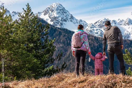 Father and mother with small child on top of Monte Nebria Est with panoramic view of snow capped mountains of Julian Alps, Friuli Venezia Giulia, Italy. Family hike in alpine wilderness in spring photo