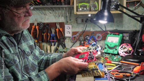 An elderly technician repairs computer equipment in a workshop using measuring instruments and technical tools. Slow motion.