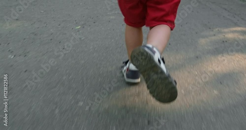 A little boy in red shorts runs along the asphalt path to his little one. Shot from behind.