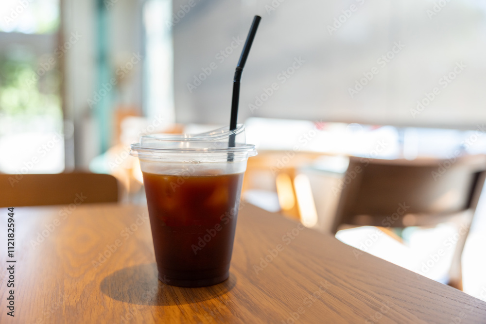 A cup of ice americano coffee with a straw in it sits on a wooden table. A cup of ice americano coffee with a straw in it sits on a wooden table.