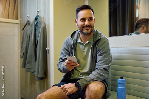 Smiling athlete using spart phone in dressing room at gym. photo