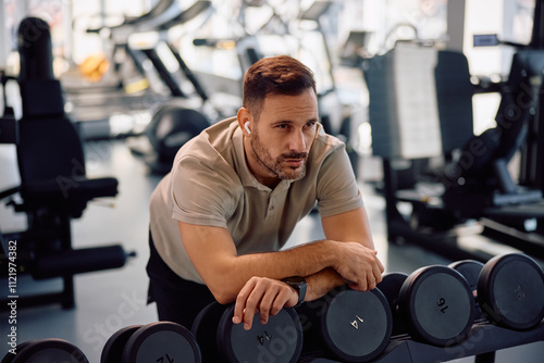 Pensive athlete taking a break during weight training in gym.