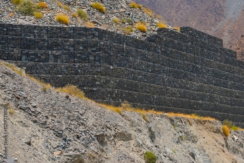 Reinforcing mountain slope with metal mesh and stone blocks, gabion wall, preventing rocks falling, shedding on road. Landslide, cliff erosion control and rock sliding prevention in UAE. photo