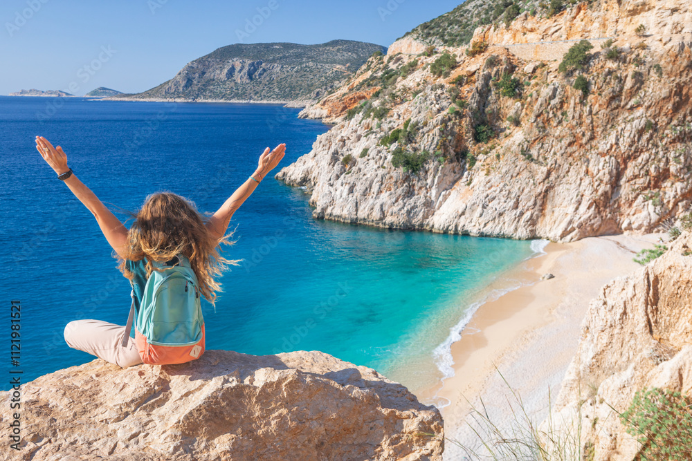 Naklejka premium Young woman with backpack looking out over Kaputas beach, Lycia coast. Summer day walk by Lycian way at family vacation in Mediterranean Sea, Kas, Antalya region, Turkey