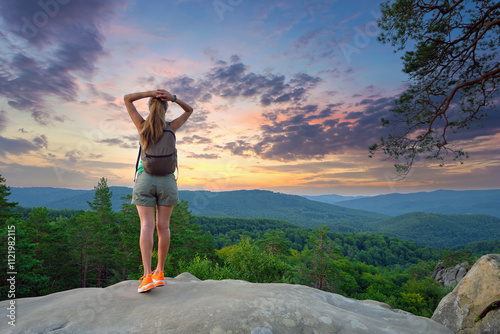 Sportive woman walking alone on hillside trail. Female hiker enjoying view of evening nature from rocky cliff on wilderness path. Active lifestyle concept