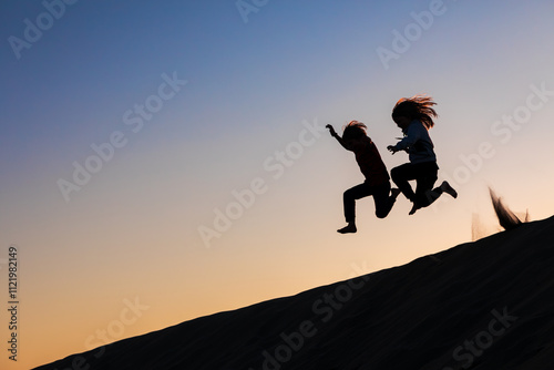 Black silhouette at sunset sky background. Happy family - kids running and jumping high in the air from sea beach sand dune. Active people, outdoor activity on tropical summer vacations with children