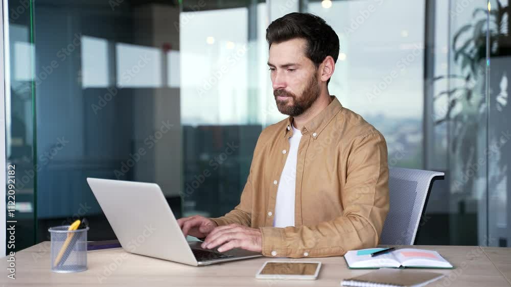Focused handsome businessman typing on a laptop sitting at a workplace in a business office. Bearded male worker working in computer, banking, texting a client, chatting online or busy with a project
