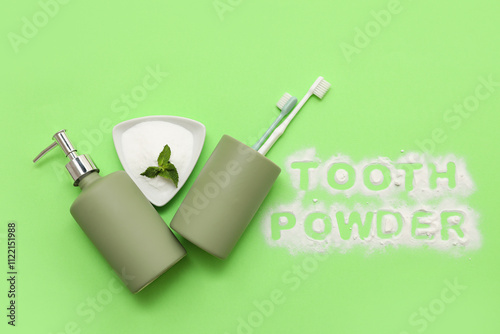 Bowl of tooth powder with mint leaf, brushes in holder, soap dispenser and text TOOTH POWDER on green background. Top view photo