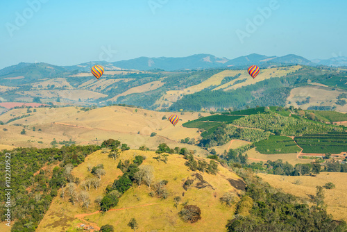 The majestic horizon features colorful balloons floating gently around the clear blue sky, creating a scene of serenity and freedom. All around, a mountainous landscape unfolds in stunning detail, whe photo