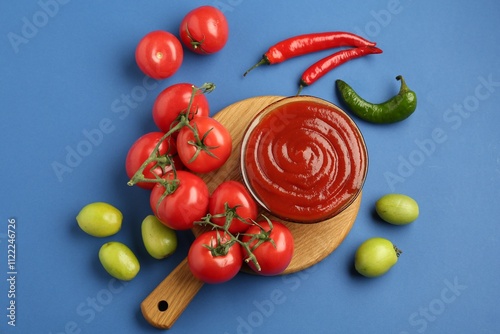 Tasty ketchup and vegetables on blue background, flat lay