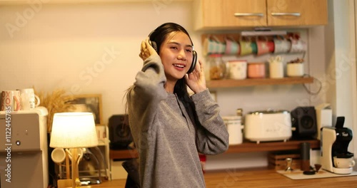 Asian student wearing headphones and drink coffee at in the kitchen
