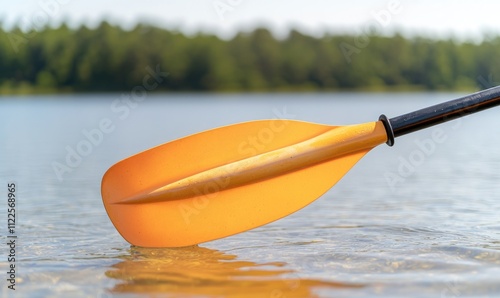A close-up of an orange kayak paddle dipping into serene water, surrounded by lush greenery.