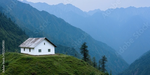 A serene white house stands atop a hill surrounded by mountains, showcasing tranquil nature and peaceful living.