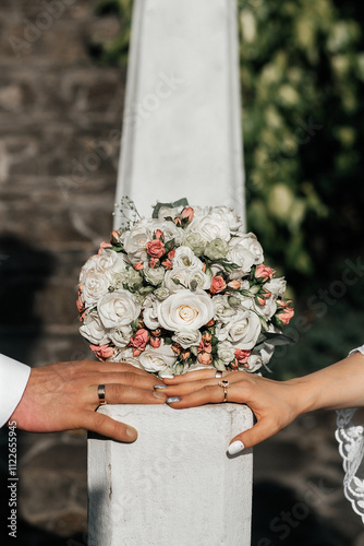 On the column is a bouquet of flowers consisting of white and pink roses. The man's hand is on the left, the woman's on the right, and there are wedding rings on both hands. photo