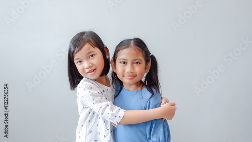 Studio portrait of Asian children on a light background, two children hugging as a best friend and smiling to the camera.