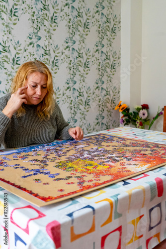 Vertical image of a pretty Caucasian woman in her 40s doing a puzzle in the living room of her home. Entertainment concept