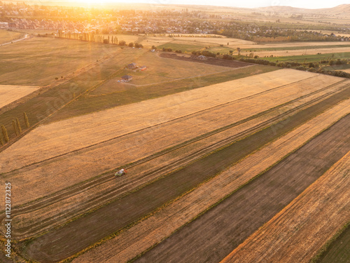 Drone photo of the tractor working in the field forming hay into briquettes in sunset time. Harvesting time. Amazing agricultural landscape with fields and nountains photo