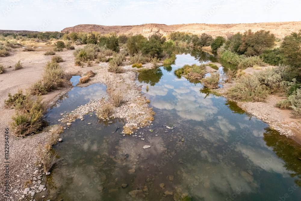 Naklejka premium Low scattered clouds are reflected in the Fish River in Southern Namibia