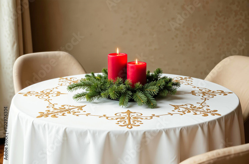 A festive centerpiece featuring red candles surrounded by fresh green pine branches on a white tablecloth with golden embroidery. Perfect for elegant holiday table settings. Selective focus photo