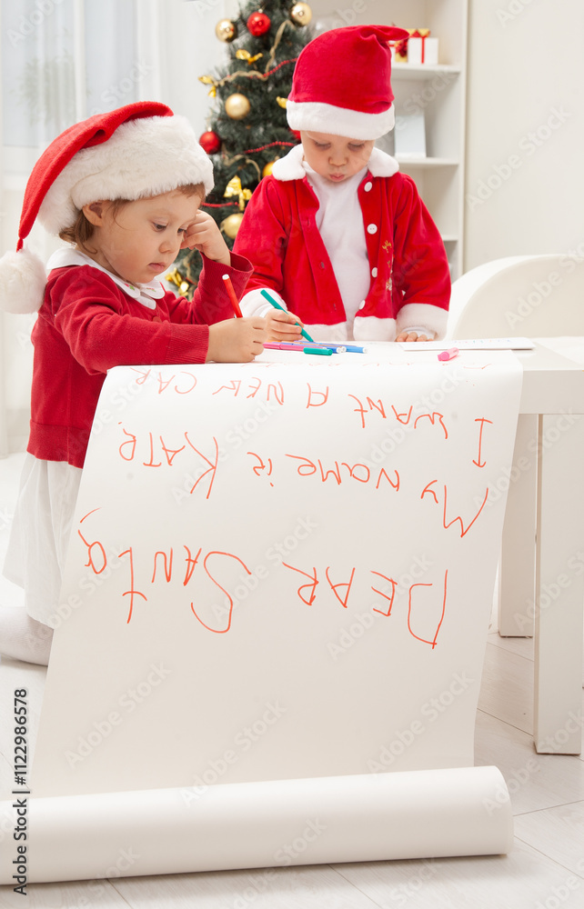 little kids in Santa hat writing letter to Santat under the Christmas tree