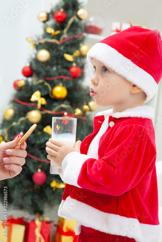 Obraz na płótnie Portrait of little cute boy in Santa hat drinking milk with biscuit w salonie