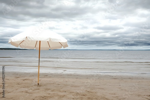 Serene Beach Scene with White Umbrella Under Overcast Sky, Calm Waters Lapping on Sandy Shore, Perfect for Summer Relaxation or Vacation Themed Projects photo