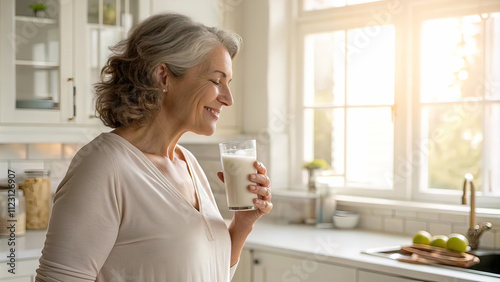 stylish middle aged woman holding glass of milk in hand in morning, woman has slim figure, on blurred light background