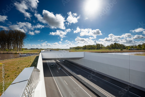 Highway overpass with modern concrete barriers, sunny day, and traffic.  Cars visible on the highway below. photo