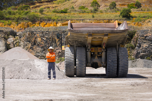 Man with arms crossed standing behind the hauler truck with massive wheels. photo