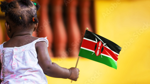 Adorable black African kid female baby todler girl standing holding Kenya national flag in hand. December 12 Independence Day celebration. back view
 photo