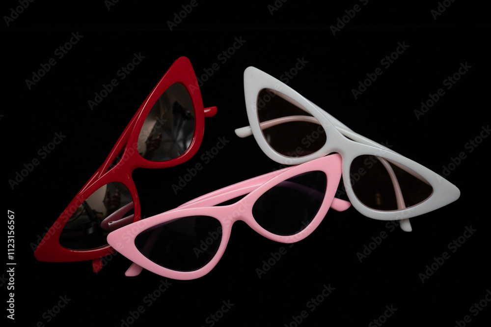three sunglasses of different colors with cat eye frames lie on a black background