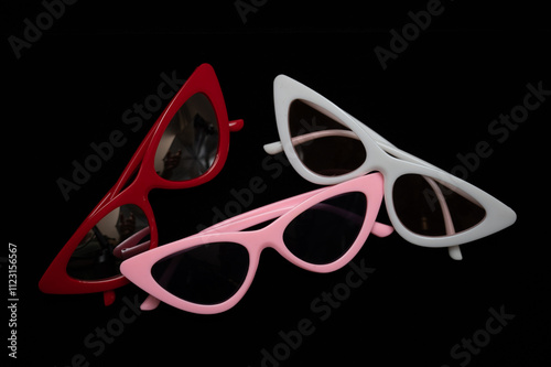three sunglasses of different colors with cat eye frames lie on a black background