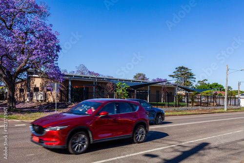 Red and blue car passing along street in town near childcare centre building photo