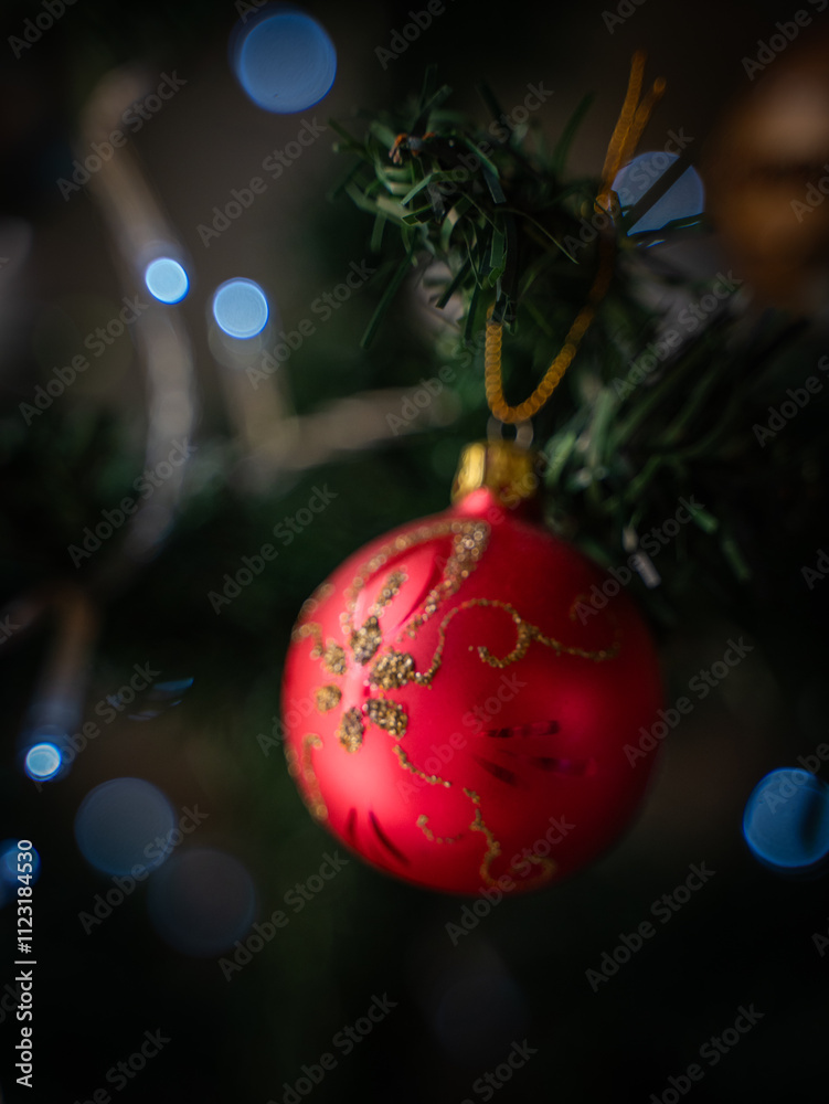 Fototapeta premium Red and gold Christmas ornament hanging on a tree with glowing lights 