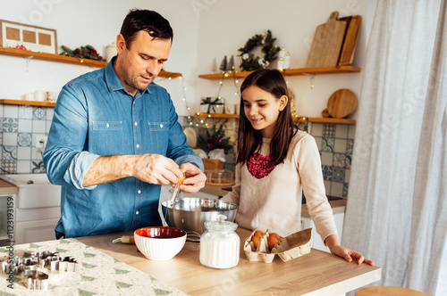 An attractive man and his sweet daughter cook together in the kitchen. A young dad teaches a teenage girl how to make cookie dough. A man breaks an egg into a bowl.