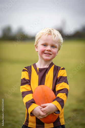 Little boy in Aussie Rules Football uniform on field with ball