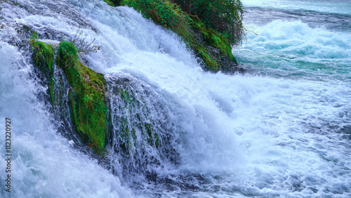 An energetic display of cascading water over moss-covered rocks in a vibrant, lush setting, capturing the power and movement of nature with invigorating energy.