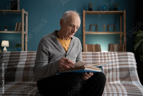 Lonely man widower looking at the photos and remembering his wife while sitting on sofa in the living room